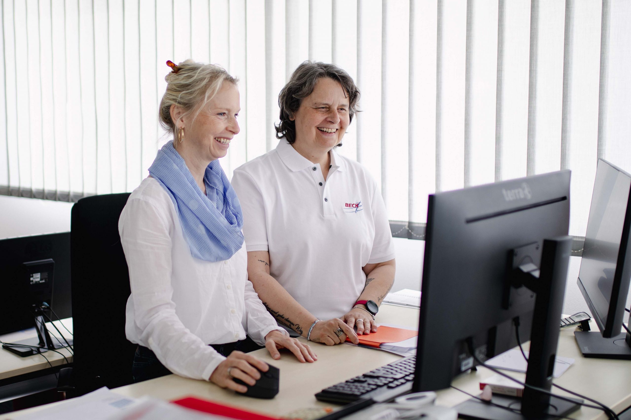 Zwei Frauen stehen an einem Schreibtisch und schauen in einen Computer.